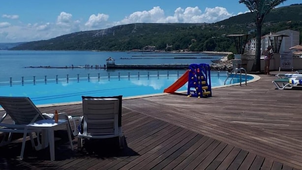 A wooden deck with lounge chairs, a pool, and a playground area.