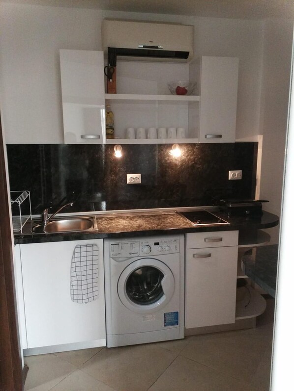 Une cuisine compacte équipée d’un lave-linge, d’un évier et d’un plan de travail.