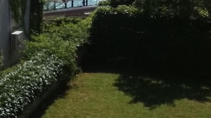 A view of a lake with a pier and a gazebo, surrounded by greenery and a building.