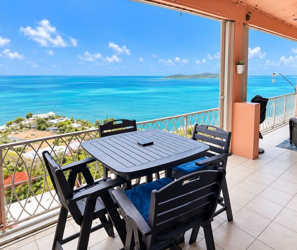 A terrace with a table and chairs, overlooking a turquoise sea and a distant island. - The Lookout-New Booking Discount--Caribbean views, pool, generator. (Christiansted)