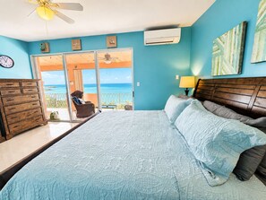 A bedroom with a bed, a dresser, a chair, and a view of the ocean through a sliding door. - The Lookout-New Booking Discount--Caribbean views, pool, generator. (Christiansted)