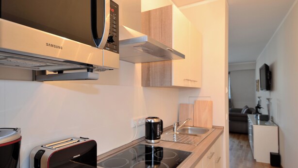 Una cucina moderna con forno a microonde, tostapane e bollitore integrati, una cappa aspirante in acciaio inossidabile e un piccolo lavandino.