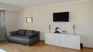 Un soggiorno moderno con un divano grigio, un mobile bianco, un televisore a schermo piatto e vasi decorativi.