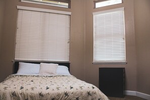 A bedroom with a bed, two windows with blinds, and a wall-mounted heater. - Madrone Manor, A Beautiful Spacious Getaway (Elverta)