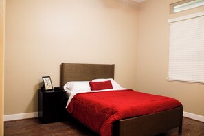 Ein Schlafzimmer mit einem Einzelbett, einem Nachttisch, einem gerahmten Bild und einem Fenster mit Jalousien.