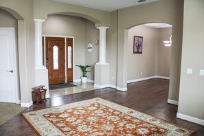 A hallway with a patterned rug, a wooden door, and a potted plant. - Madrone Manor, A Beautiful Spacious Getaway (Elverta)