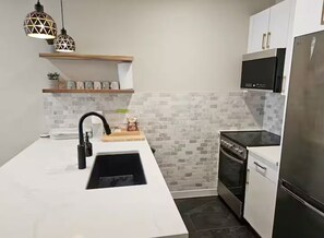 A modern kitchen with a white countertop, a black sink, a stove, a refrigerator, and a TV mounted above the stove. - NEW! Whistler Village Family Condo | Mountain Views + Hot Tub + Free Parking (Whistler)