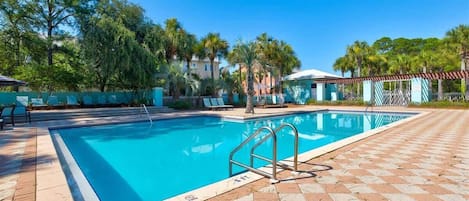 A swimming pool with a tiled deck, lounge chairs, and palm trees in the background.