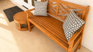 Un banc en bois avec des coussins à motifs, une petite table ronde et un luminaire fixé au mur.