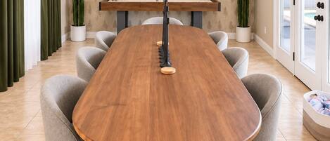 A dining room with a wooden table, grey upholstered chairs, a ceiling fan, and a patterned wallpaper.