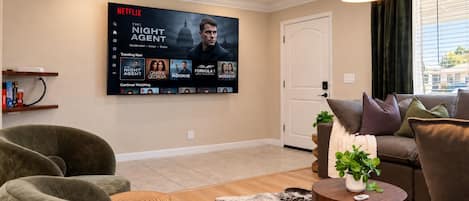 A living room with a large flat-screen TV displaying a Netflix interface, a sofa, a coffee table, and a ceiling fan.