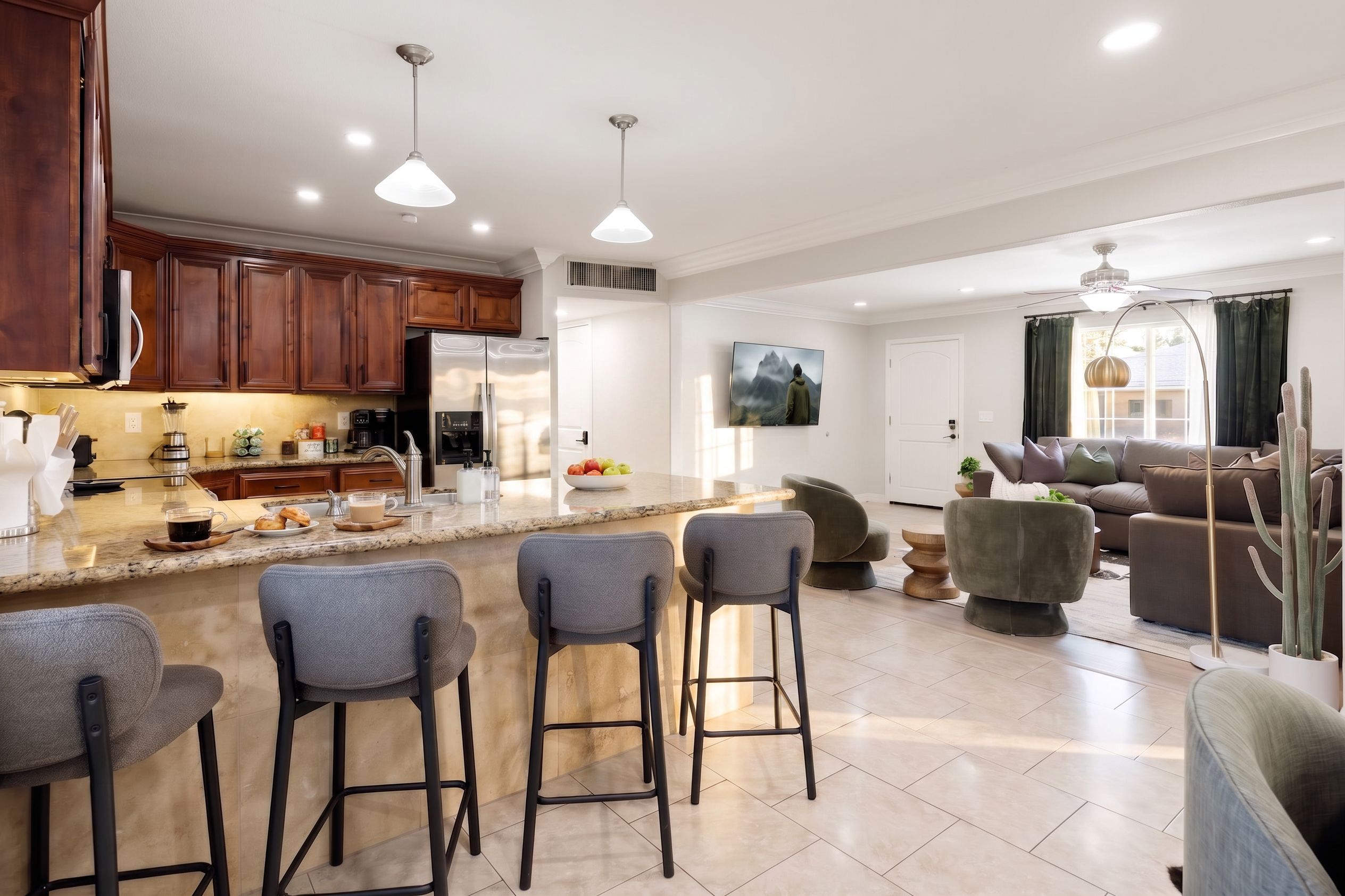 A modern kitchen with a central island, bar stools, and a dining area with a sofa and chairs.