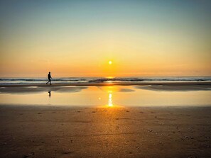 A beach with a person walking, reflecting the sunset on the wet sand. - Ocean View Studio • Pool Sleeps 4 (Daytona Beach)