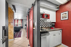 A kitchen with a red and white color scheme, a checkered backsplash, and a framed NASCAR poster. - Ocean View Studio • Pool Sleeps 4 (Daytona Beach)