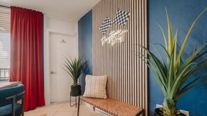 A room with a bench, a potted plant, a wall with vertical stripes, and a neon sign.