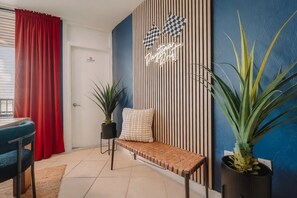 A room with a bench, a potted plant, a wall with vertical stripes, and a neon sign.