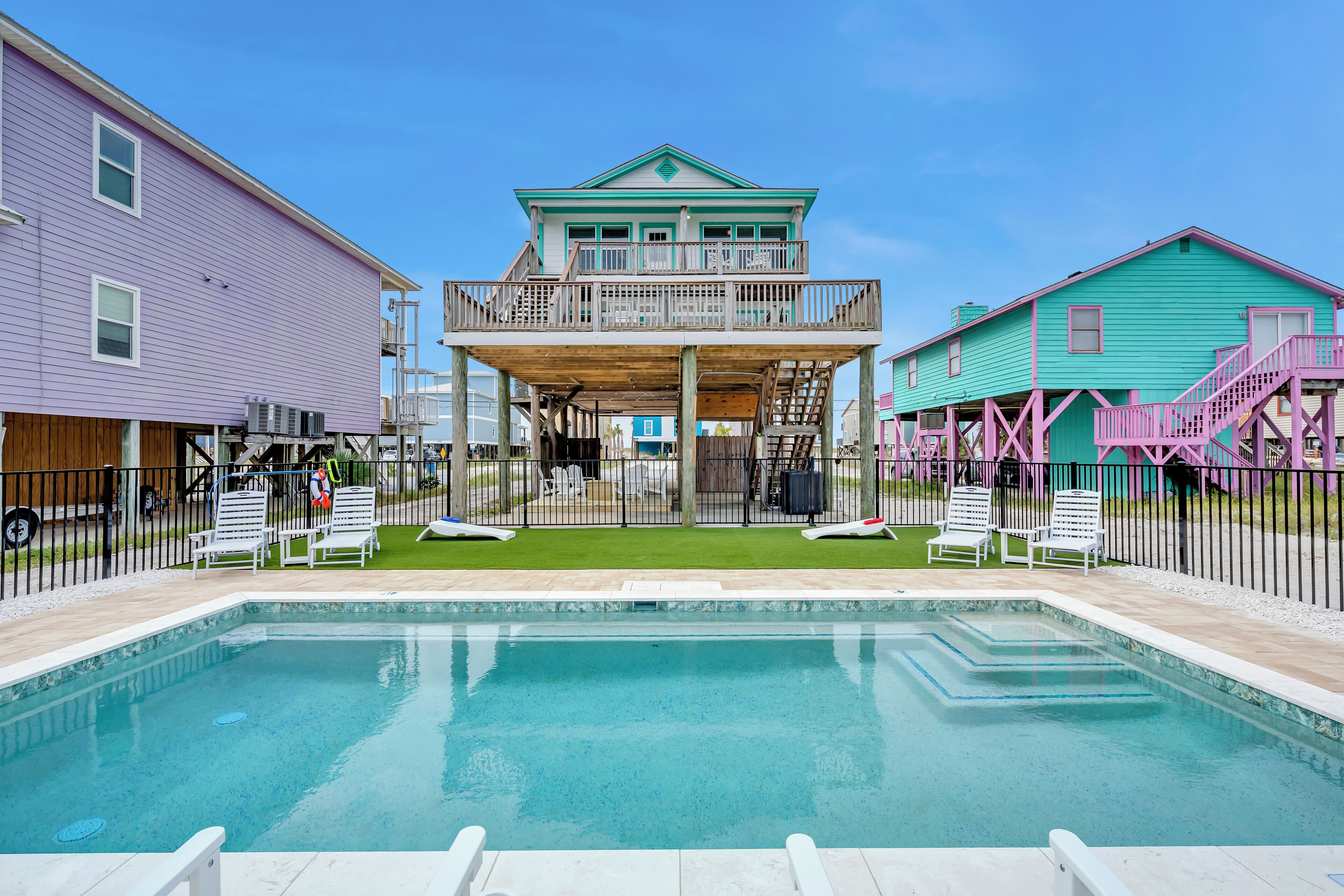 A swimming pool with a wooden deck, surrounded by a fence, and adjacent to a building with a balcony.