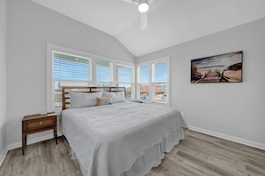 Ein Schlafzimmer mit einem großen Bett, einem Nachttisch, einem Deckenventilator und einem Wandbild mit Strandmotiv.