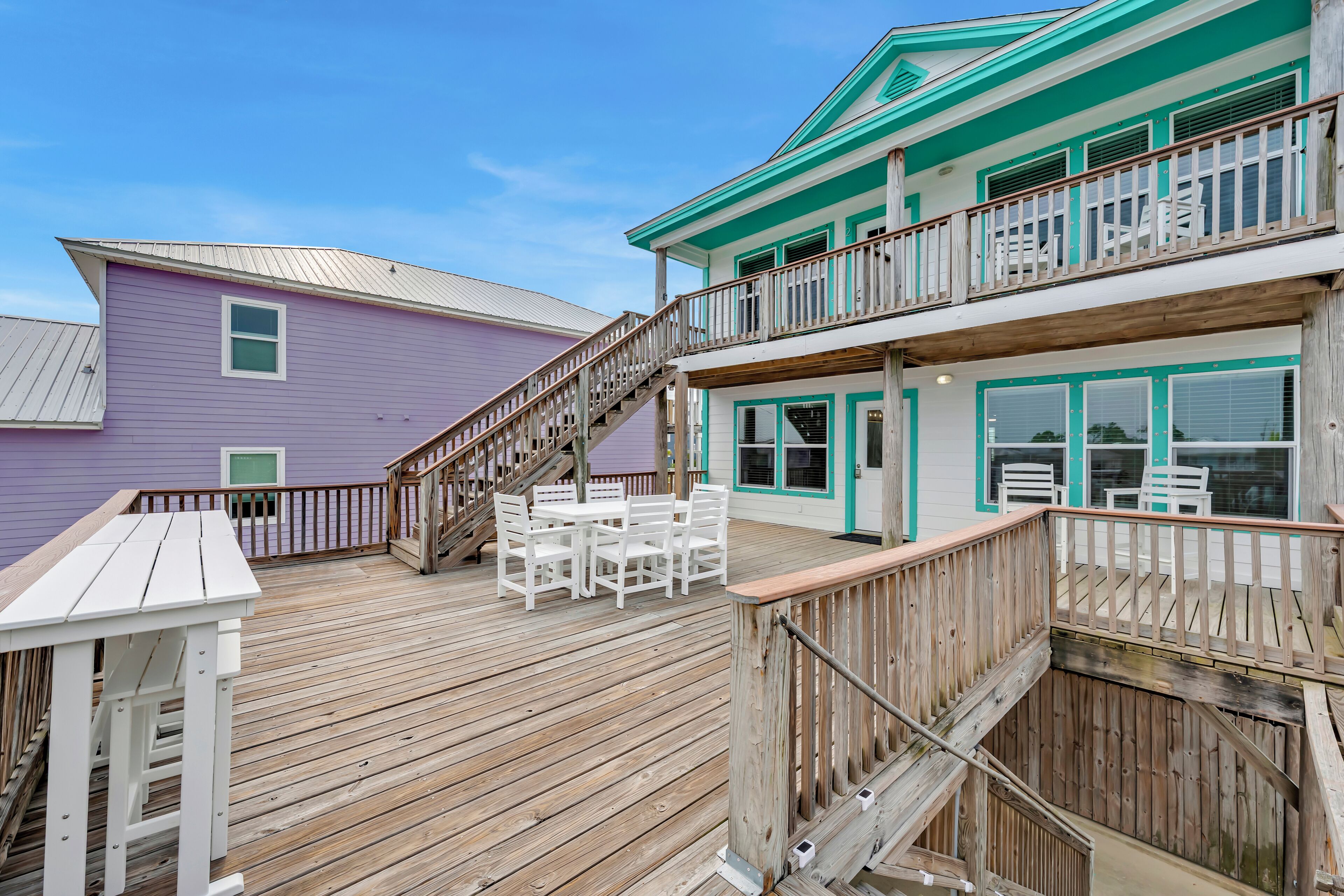 A wooden deck with outdoor furniture, a staircase, and a two-story building with a balcony.