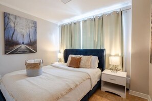 A bedroom with a bed, nightstands, a lamp, a painting, and curtains. - Elegant Stay in Montréal (Montreal)