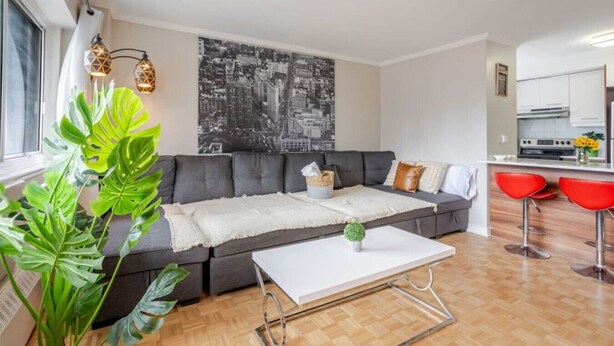 Ein modernes Wohnzimmer mit grauem Sofa, einem weißen Couchtisch und einer Stadtlandschaft als Wandbild.