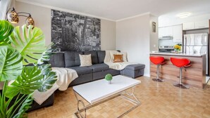 Ein modernes Wohnzimmer mit einem grauen Sofa, einem weißen Couchtisch und einer Stadtansicht als Wandbild.