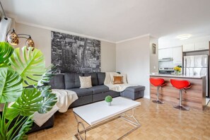 Ein modernes Wohnzimmer mit einem grauen Sofa, einem weißen Couchtisch und einer Stadtansicht als Wandbild.