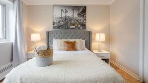 Ein Hotelzimmer mit einem großen Bett, zwei Nachttischlampen, einem Wandbild und einem Fenster mit Vorhängen.