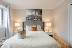 Ein Hotelzimmer mit einem großen Bett, zwei Nachttischlampen, einem Wandbild und einem Fenster mit Vorhängen.