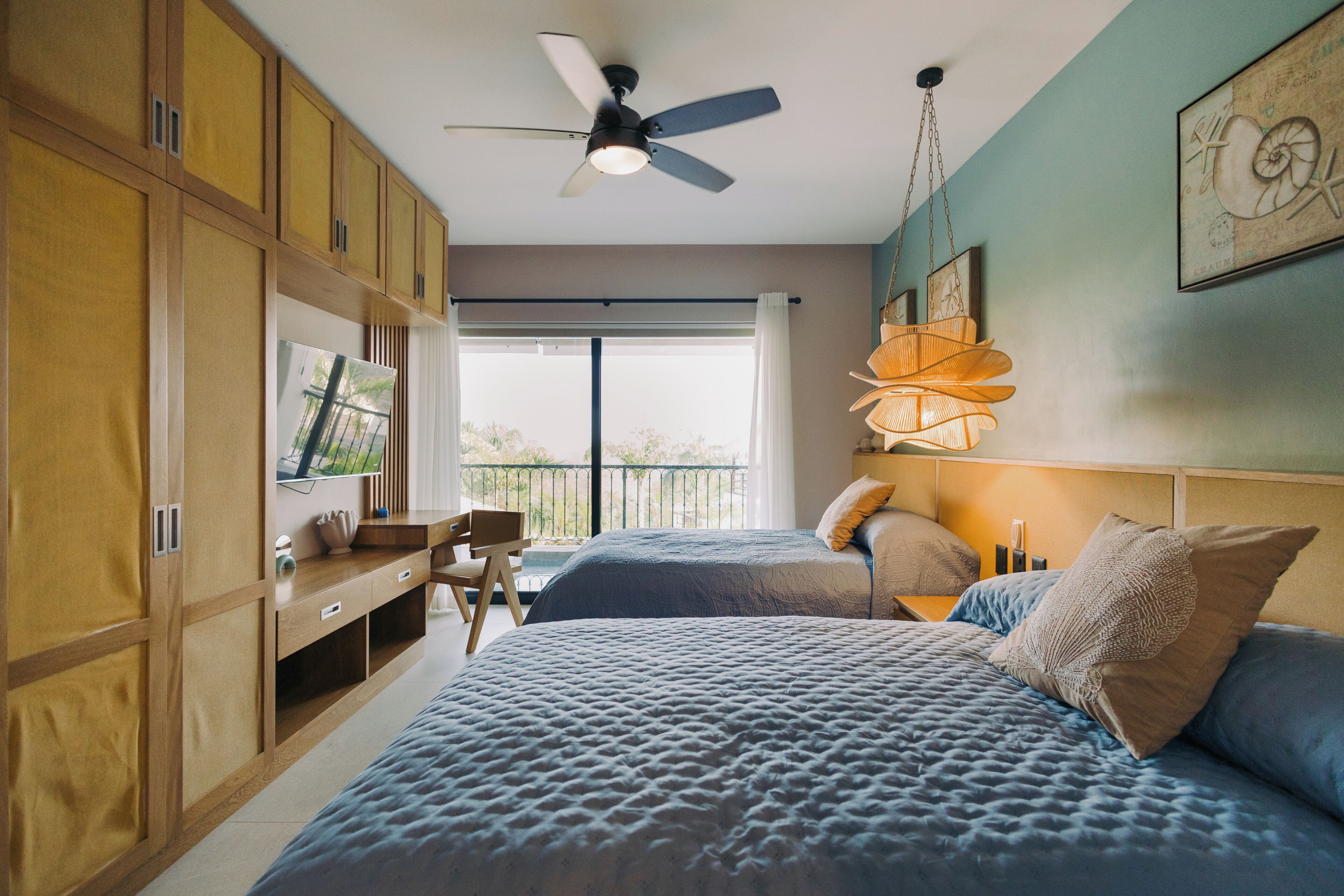A bedroom with a bed, a desk, a chair, a ceiling fan, and a window.