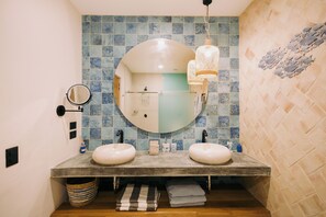 Casa de banho com duas pias, um espelho grande e parede revestida a azulejos.