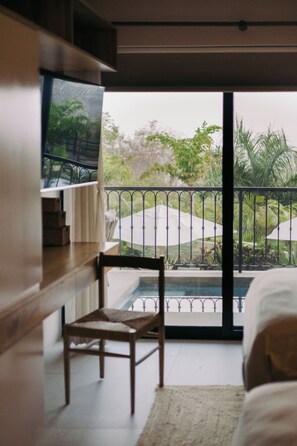 Quarto com vista para uma piscina e jardim, uma cadeira de madeira e uma cama.