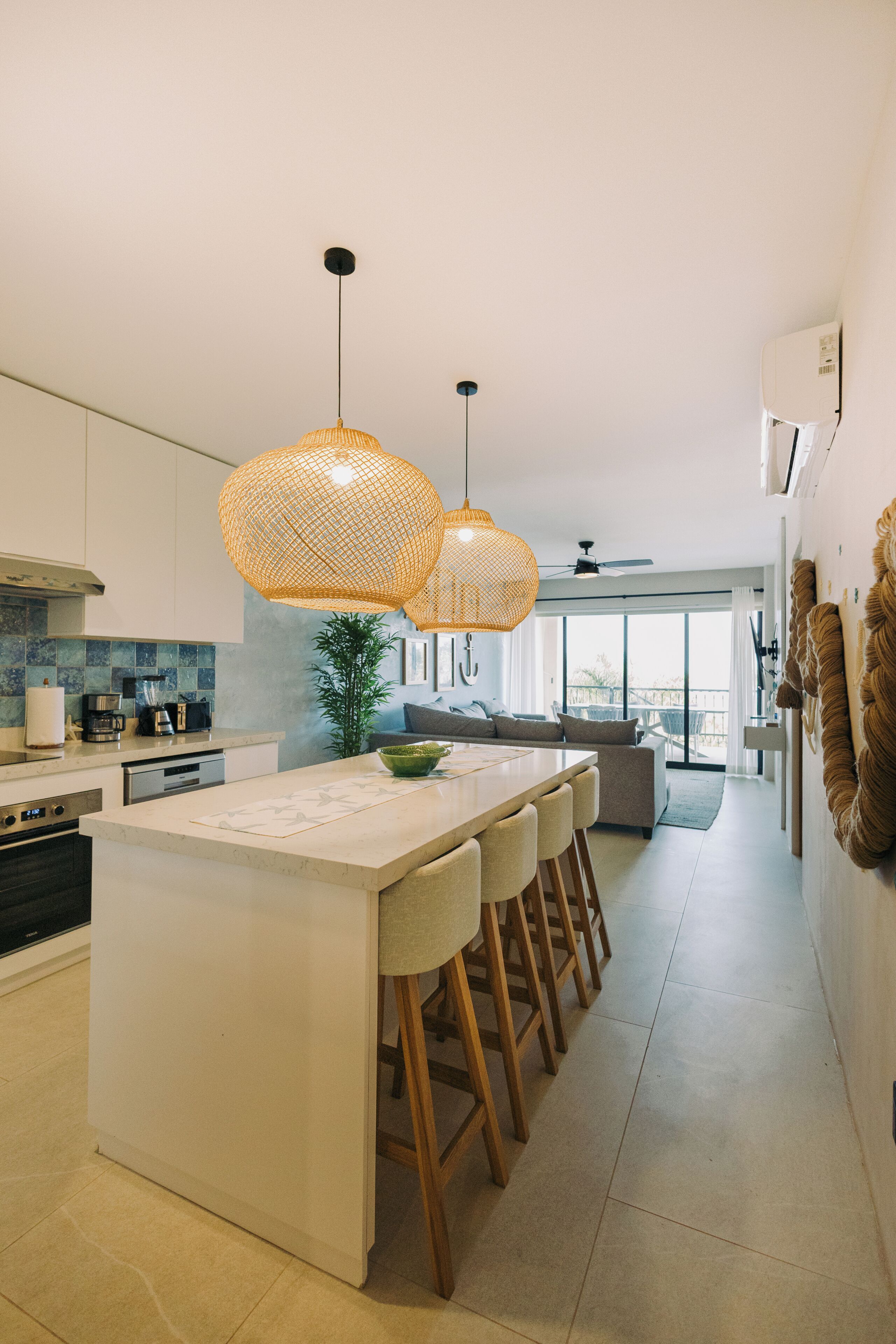 Een moderne keuken met een centraal kookeiland, een bar met krukken, hanglampen en uitzicht op de woonkamer.