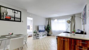 Ett modernt vardagsrum med TV, matplats och ett stort fönster med gardiner.