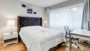 Ett hotellrum med en säng, ett skrivbord, en stol, ett nattduksbord och en lampa.