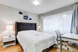 Ein Hotelzimmer mit Bett, Schreibtisch, Stuhl, Nachttisch und Lampe.