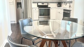 Une cuisine moderne avec des meubles blancs, des appareils en acier inoxydable et une table à manger en verre.