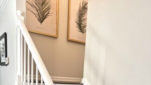 Un escalier avec des balustrades blanches et des marches sombres, menant à un palier orné de reproductions botaniques encadrées sur le mur.