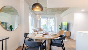 A modern dining area with a round table, black chairs, a large mirror, and a pendant light.
