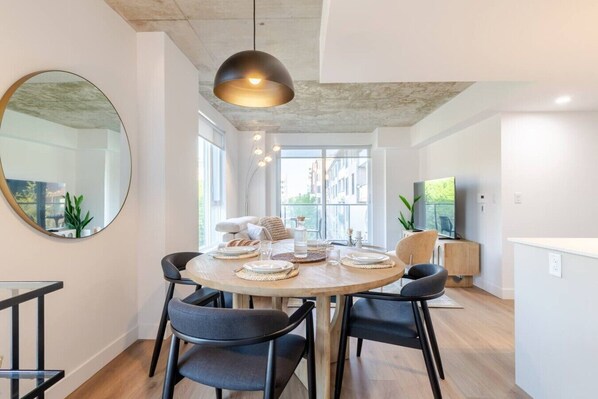 A modern dining area with a round table, black chairs, a large mirror, and a pendant light.