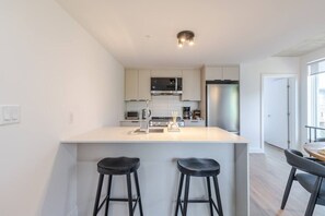 A modern kitchen with a central island, two bar stools, and a dining area with a table and chairs.