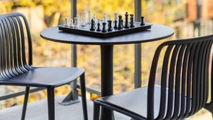 Schaakbord op een balkon met stoelen, met uitzicht op een stadsbeeld vol gebouwen en herfstkleuren.