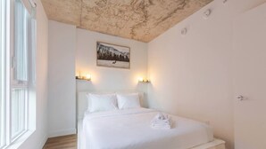 Een slaapkamer met een bed, een schilderij erboven en een deur aan de rechterkant.