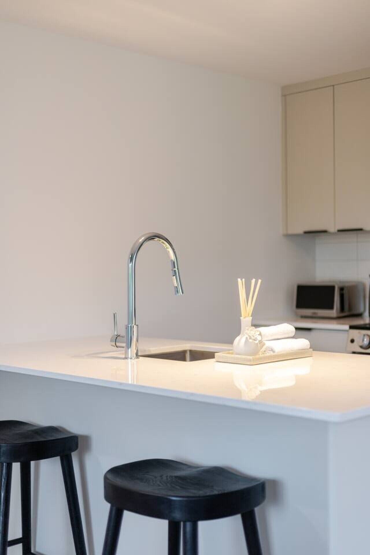 Een moderne keuken met een wit aanrecht, een roestvrijstalen kraan en twee zwarte krukken.
