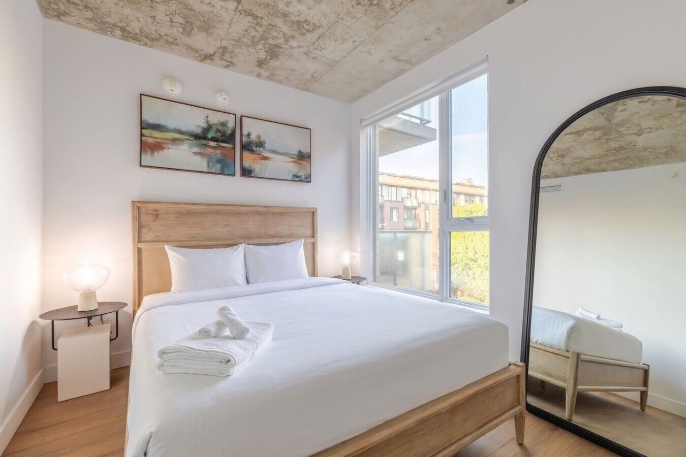 Een slaapkamer met een bed, nachtkastjes, een groot raam en een spiegel.