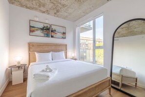 Ein Schlafzimmer mit einem Bett, Nachttischen, einem großen Fenster und einem Spiegel.
