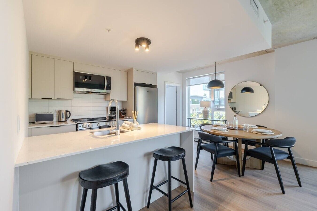 Een moderne keuken met een centraal eiland, barkrukken en een eethoek met een ronde tafel en stoelen.