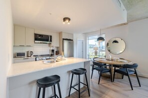 A modern kitchen with a central island, bar stools, and a dining area with a round table and chairs. - Grand Horizon Montréal | Free Parking (Montreal)