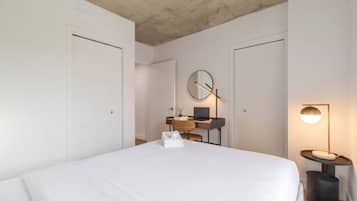 A bedroom with a bed, a desk with a laptop, a round mirror, and a bedside lamp.