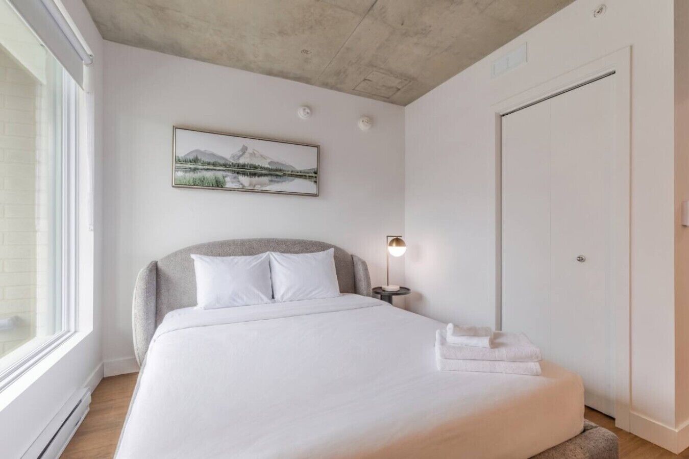 Ein Schlafzimmer mit Bett, Nachttisch, Lampe, einem Bild und einer Tür.
